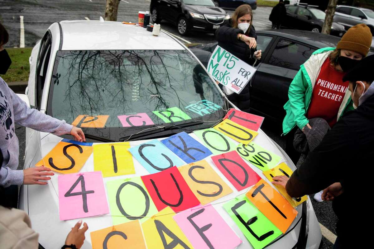 (From left) Garfield Elementary fifth grade teacher Natalie Canellas, Garfield Elementary fourth and fifth grade teacher Carrie Lanheer and second grade teacher Alex Brandenburg decorate Garfield Elementary third grade teacher Kiana Pineda's car before participating in a car caravan demonstration leaving from the Leona Canyon Trailhead to Oakland Unified School District's downtown office in Oakland, Calif. Friday, Jan. 7, 2022. Some Oakland Unified teachers called a sickout on Friday, January 7, saying they don't feel safe teaching. They're calling for two weeks of remote learning during the latest Omicron surge.