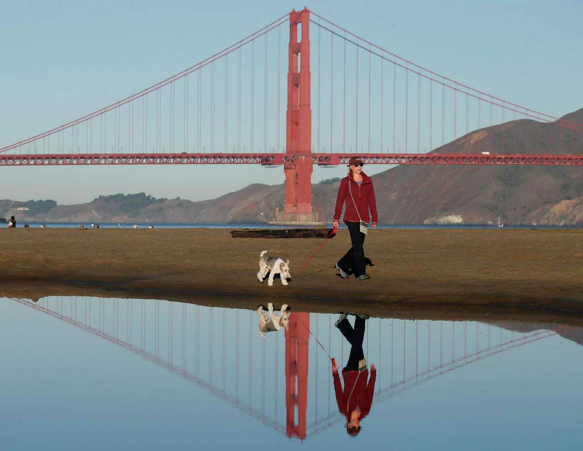 Daphne Stumpel walks on the beach with her dog Gigi at Crissy Field in San Francisco. Forecasters are predicting a week of dry and sunny conditions, with mild temperatures. Scant rain is predicted for the rest of the month.