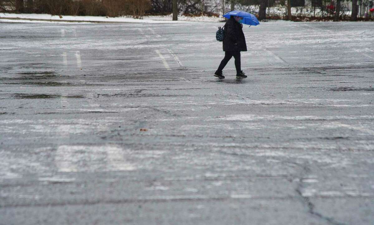 A person uses and umbrella to stay dry as they walk across an ice covered parking lot on Sunday, Jan. 9, 2022, in Albany, N.Y.