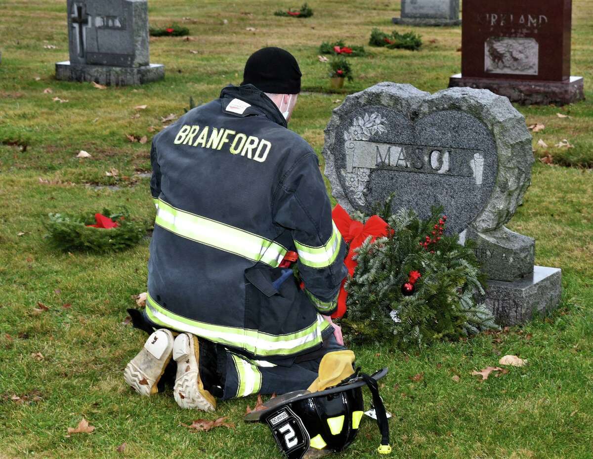 Firefighter Jeff Marci kneels to place a wreath on his granddad’s grave in Branford, when some 500 wreaths were places on veteran’s graves in Branford as part of Wreaths Across America and a local Eagle Scout project.