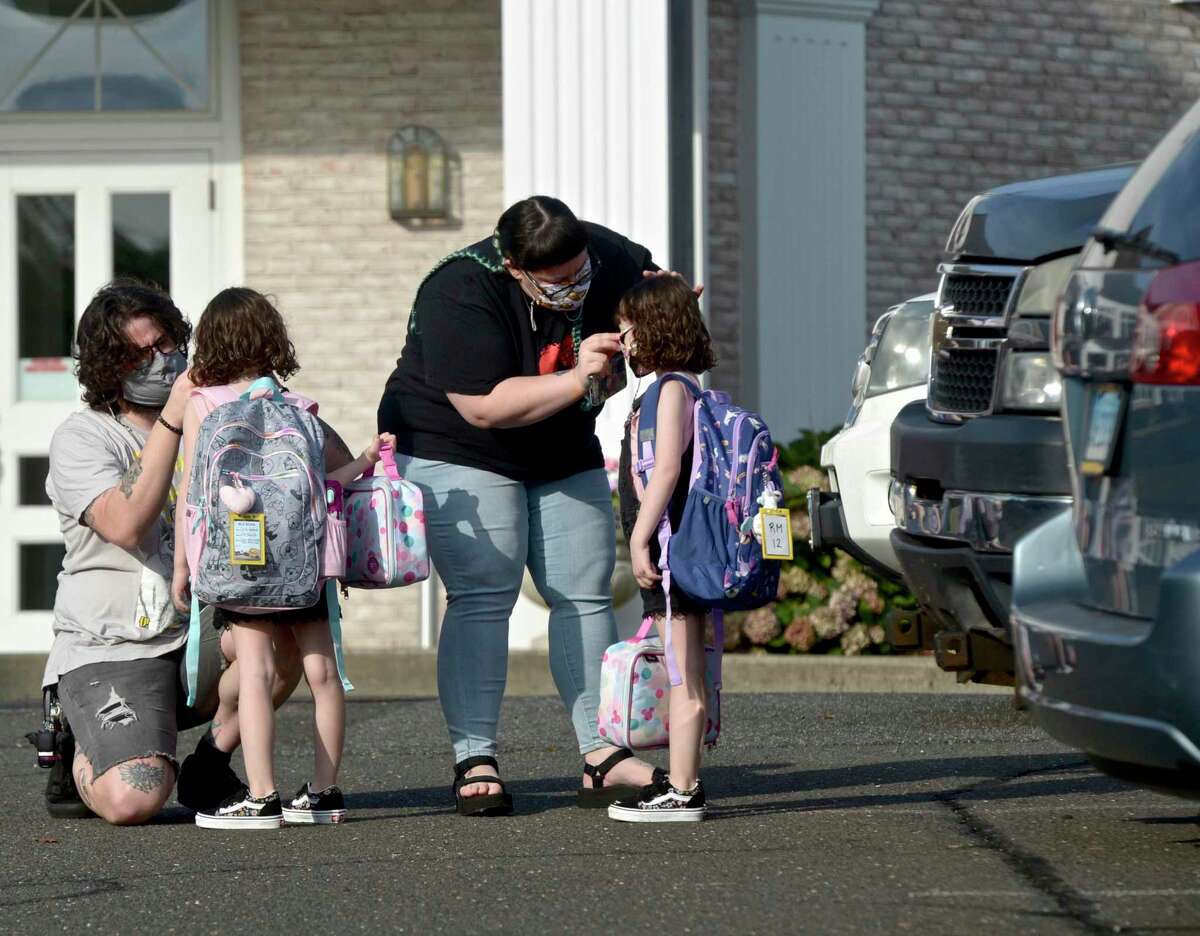 Ian Copland, left, and Megan Tucker, of Danbury, adjust their twin daughters Lilith, left, and Lydia Copland masks while dropping them off for the first day of kindergarten at the Danbury Primary Center in Brookfield. Monday, August 30, 2021, Brookfield, Conn. Some are calling for schools to be permitted to temporarily go to remote learning due to the COVID surge and staff shortages.
