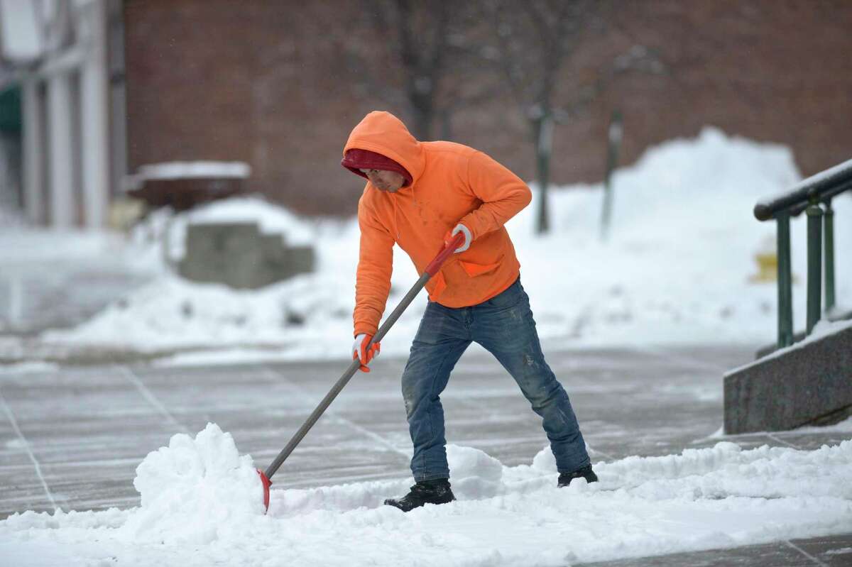 Jorge Sunva, of Danbury, shovels snow from the sidewalk in front of St Peter Church.