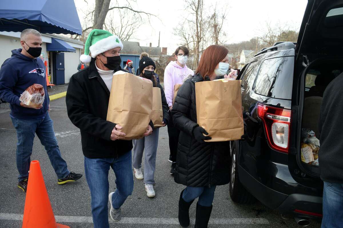 Volunteers deliver bags of food to waiting drivers during St. Vincent de Paul Food Bank’s holiday food and present pickup in Derby, Conn. Dec. 21, 2021.