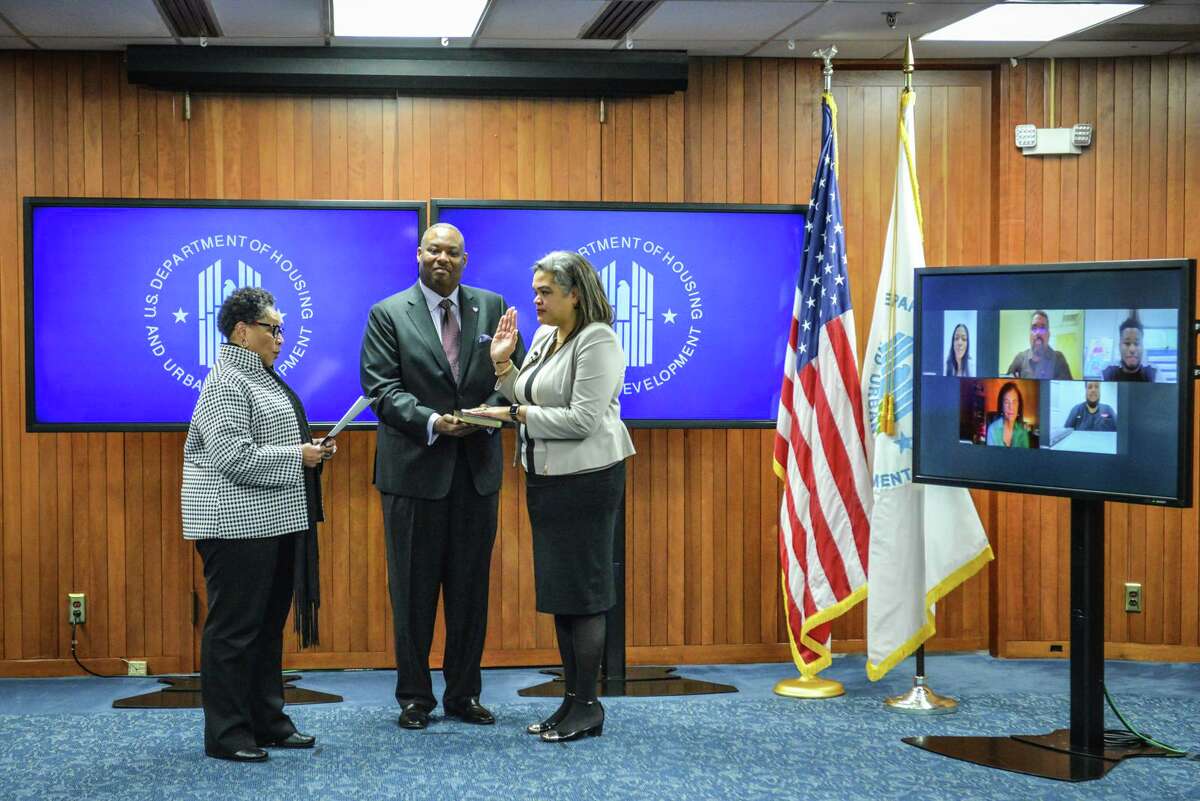 Alanna McCargo stands with her husband (center) as she is sworn in by HUD Secretary Marcia L. Fudge (left) on Dec. 16, 2021. McCargo's family watches virtually.