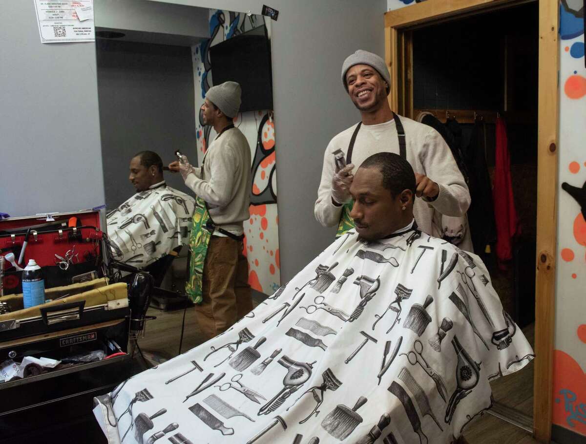 Yusuf Burgess laughs with other barbers as he cuts Jeff Jackson’s hair in Hair We R’ barber shop located on South Pearl St. on Thursday, Jan. 13, 2022 in Albany, N.Y.