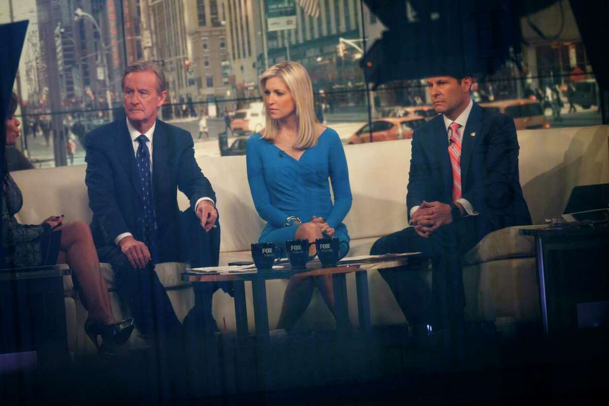 In this file photo, seen through a window, (L to R) hosts Steve Doocy, Ainsley Earhardt, and Brian Kilmeade broadcast 'Fox And Friends' from the Fox News studios, February 17, 2017 in New York City. Fox News Media is planning cuts to its staff of hair and makeup departments as part of a larger reorganization across the division. (Drew Angerer/Getty Images/TNS)