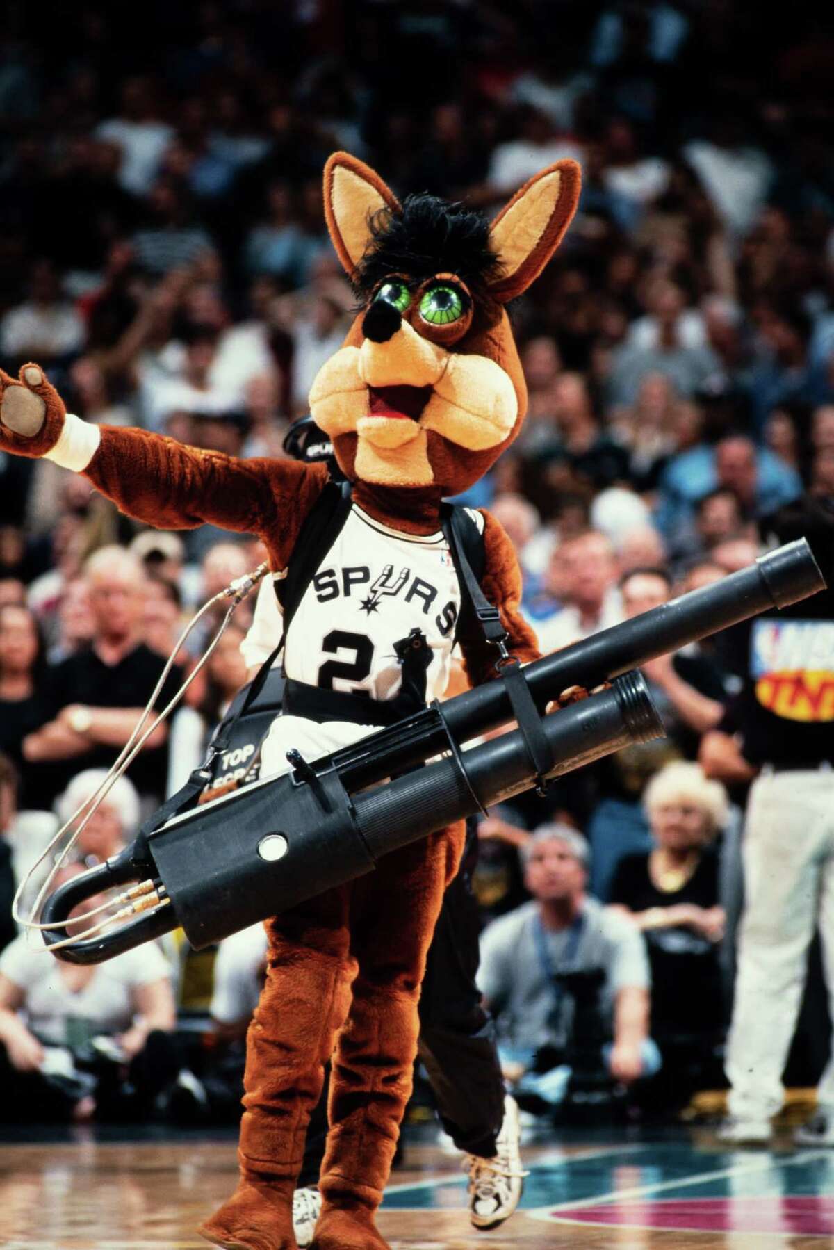 Tim Derk as the Spurs Coyote, shoots a T-shirt into the stands during a game with an early iteration of the T-shirt cannon. Derk appeared at more than 1,110 Spurs games from 1983 to 2004 and was instrumental in the development of the T-shirt cannon, the propulsive device that is now ubiquitous at most sporting events.