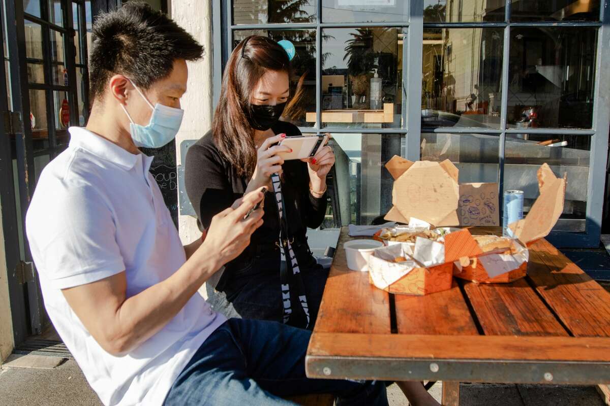 Customers Johnson Hsieh (left) and Shelley Chang photograph their order at the outdoor seating at Grégoire take-out restaurant in Berkeley, Calif. on Jan. 12, 2022.