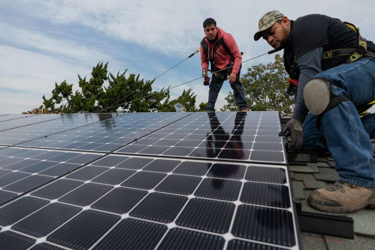 Jesus Perez (left) and Elvin Ramirez-Castro with Save A Lot Solar, secure the final panel of a solar array on the roof of a home in Oakland on Thursday, Jan. 13.