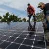 Jesus Perez, left, and Elvin Ramirez-Castro, right, with Save A Lot Solar, secure the final panel of a solar array on the roof of a home in Oakland on Thursday, Jan. 13.
