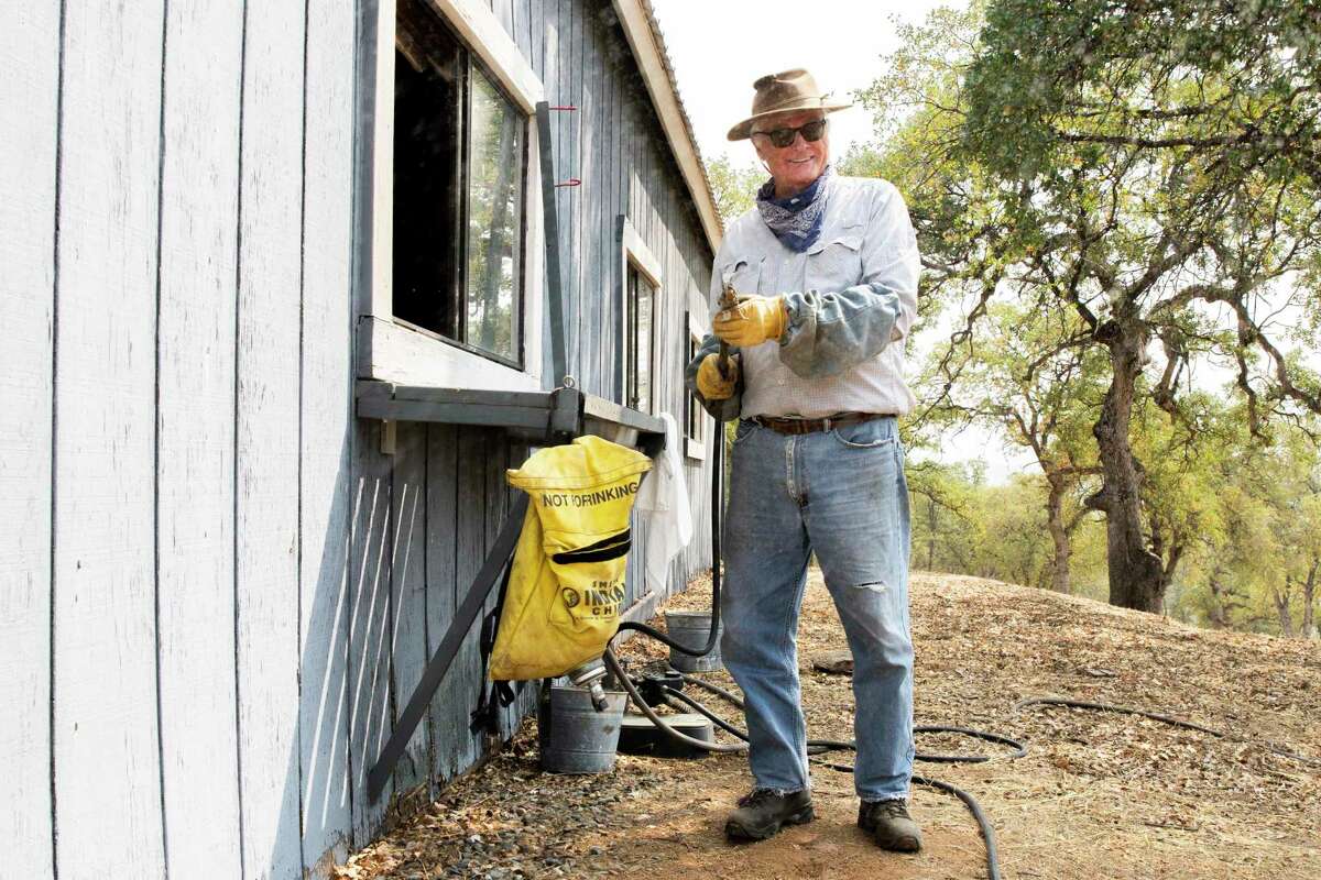William Alsup holds a hose connected to a firefighting backpack filled with water at his ranch in the Sierra Nevada.