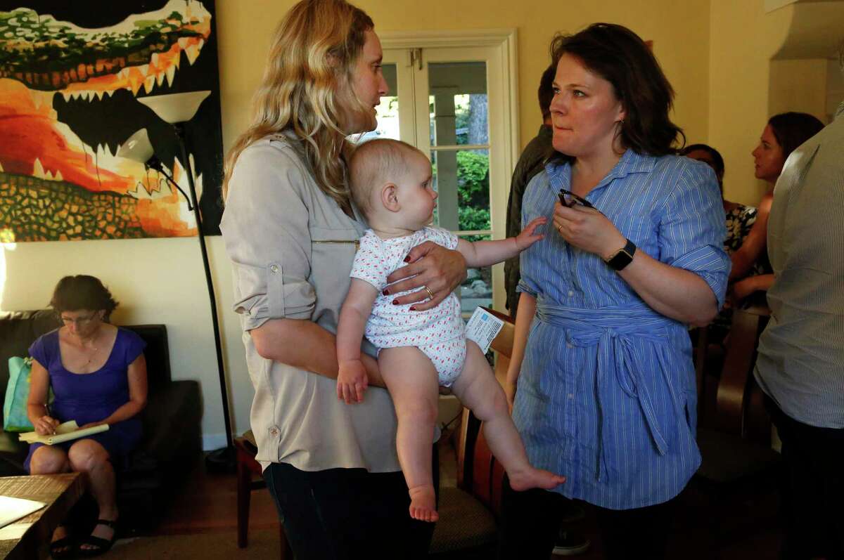 Buffy Wicks holds daughter Jojo Ambler, 7 months, as she chats with Oaklander Amy Mains after addressing the room during a 2017 political house party in Oakland.