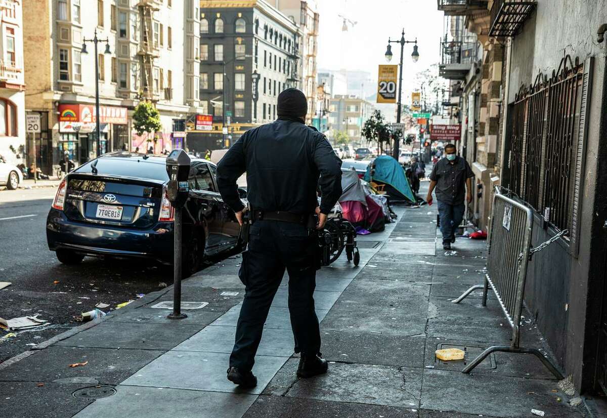 A San Francisco police officer patrols near a row of tents along Hyde Street in the Tenderloin. More outreach is being done in the troubled neighborhood.
