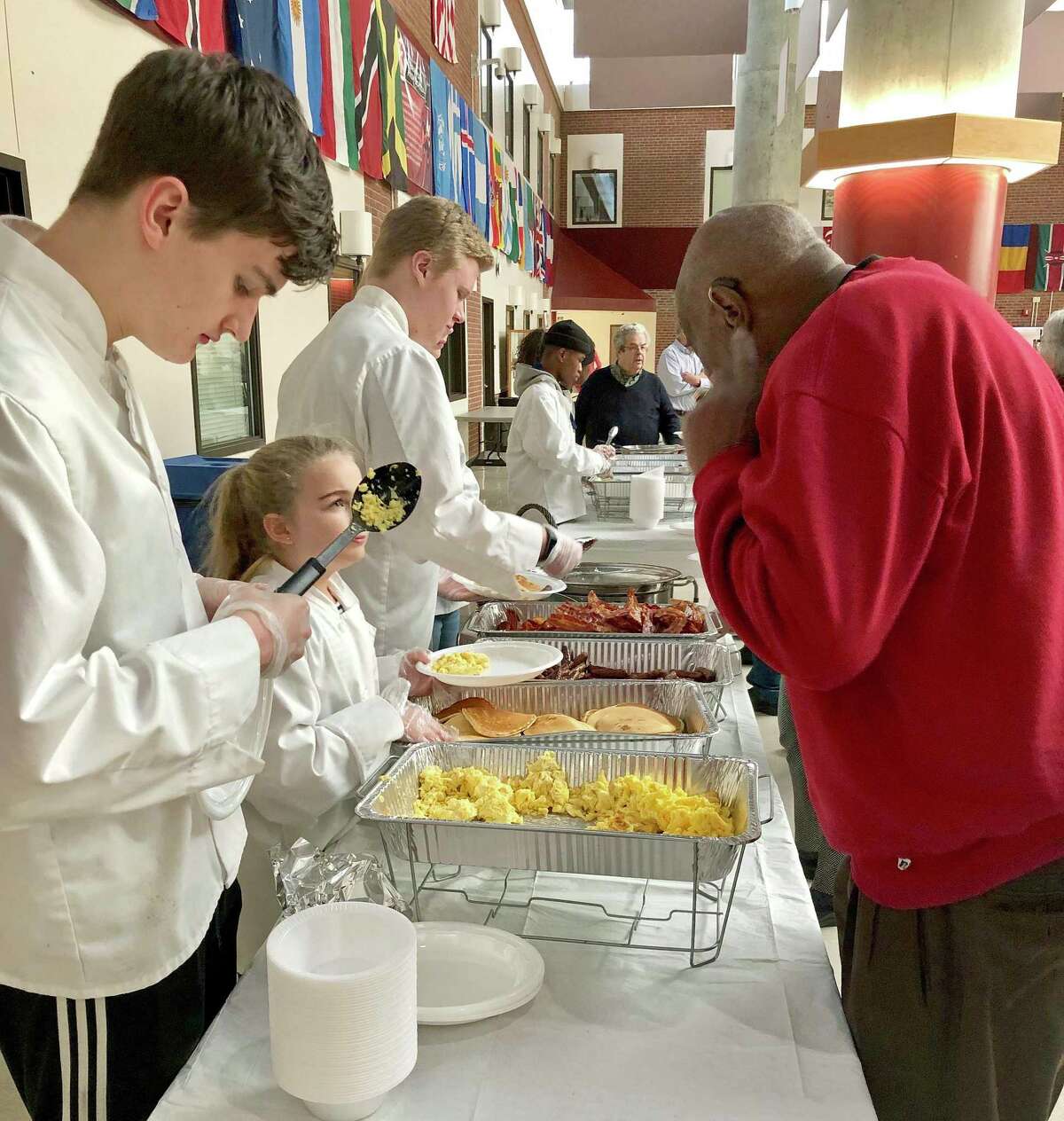 Paige Baker of Walsh Intermediate School serves pancakes to former Branford police chief Robert Gill at the annual Martin Luther King Jr. Day breakfast held, for the first time, at Branford High School on Jan. 21. In inspiring remarks, guest speaker Beth Chandler asked the roughly 225 breakfast-goers to consider “building a connection this year with at least one person who’s different from you.” Branford High School students Jack Brown and Jason Johnson are also pictured.