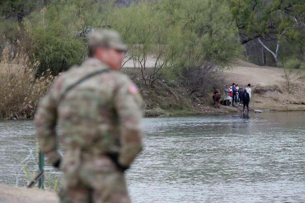 A Texas National Guard soldier stands on the banks of the Rio Grande in Eagle Pass, as migrants attempt to cross from Mexico on Wednesday. The migrants were hoping to get to a boat ramp on the U.S. side, an area not protected by fencing, but were turned away by Mexican officials and soldiers.
