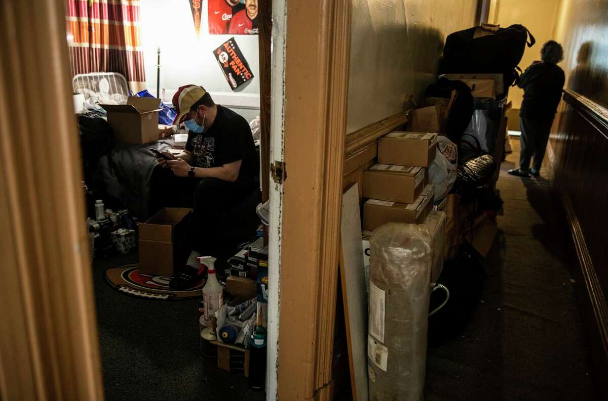 Humberto "Bob" Navarro checks his phone while packing belongings into a box as master tenant Maria Carvajal walks along a hallway with boxes in their home in San Francisco, California Saturday, Jan. 15, 2022. Navarro, a Mission native and disabled law enforcement veteran, and 81-year-old Carvajal are facing Ellis Act eviction.