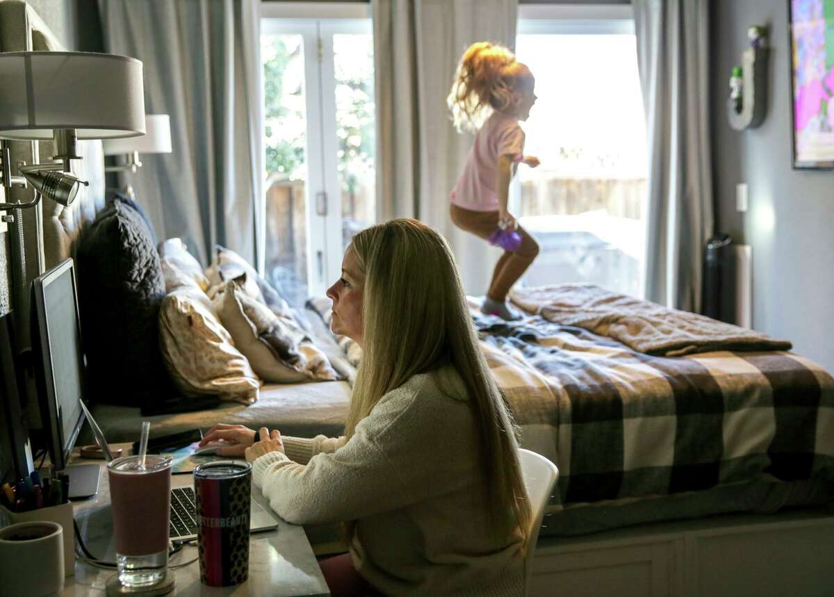 Michelle Caruso works on her computer while her four-year-old daughter jumps on her bed at their home in Livermore, Calif. 