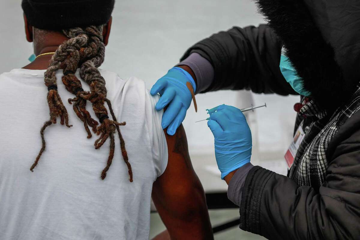 A man receives his vaccine for COVID-19 from medical assistant Tiffany Washington (right) outside non-profit Serenity House on Friday, Jan. 7, 2022 in Oakland, California.
