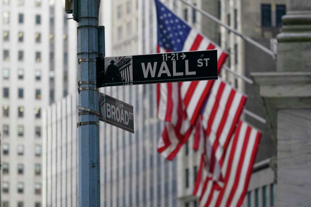 The Wall St. street sign is framed by the American flags flying outside the New York Stock exchange, Friday, Jan. 14, 2022, in the Financial District. Stocks fell broadly in morning trading on Wall Street Tuesday as investors review the latest batch of corporate earnings and continue monitoring rising inflation and the virus pandemic. (AP Photo/Mary Altaffer)