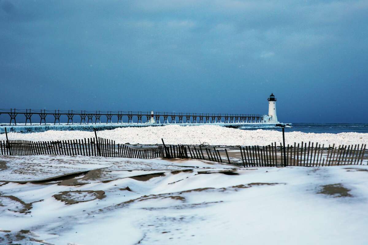 The view of the Manistee North Pier Head from the parking lot of Fifth Avenue Beach shows extensive snow and ice that covers what used to be sand and rocks. Chunks of ice also float in parts of the lake next to the pier. 