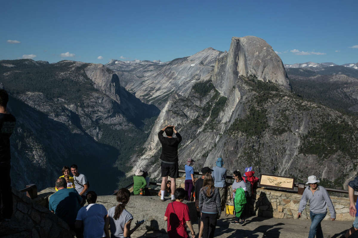 People take pictures at Glacier Point with Half Dome as a backdrop on July 1, 2019, in Yosemite Valley, California.