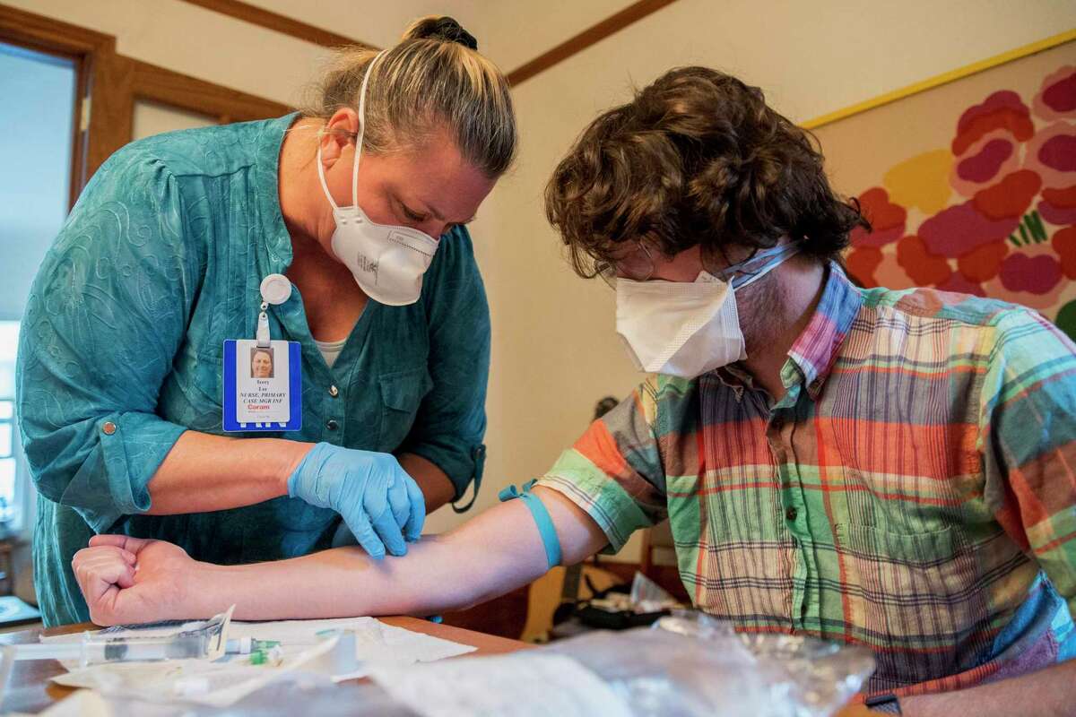 Terry Lee (left), a nurse, administers an IV treatment to Charlie McCone at his home, Thursday, Jan. 20, 2022, in San Francisco. McCone tested positive for the novel coronavirus in March 2020 and has had severe symptoms ever since. The IV fluids help treat his lightheadedness, chest pain and other symptoms.