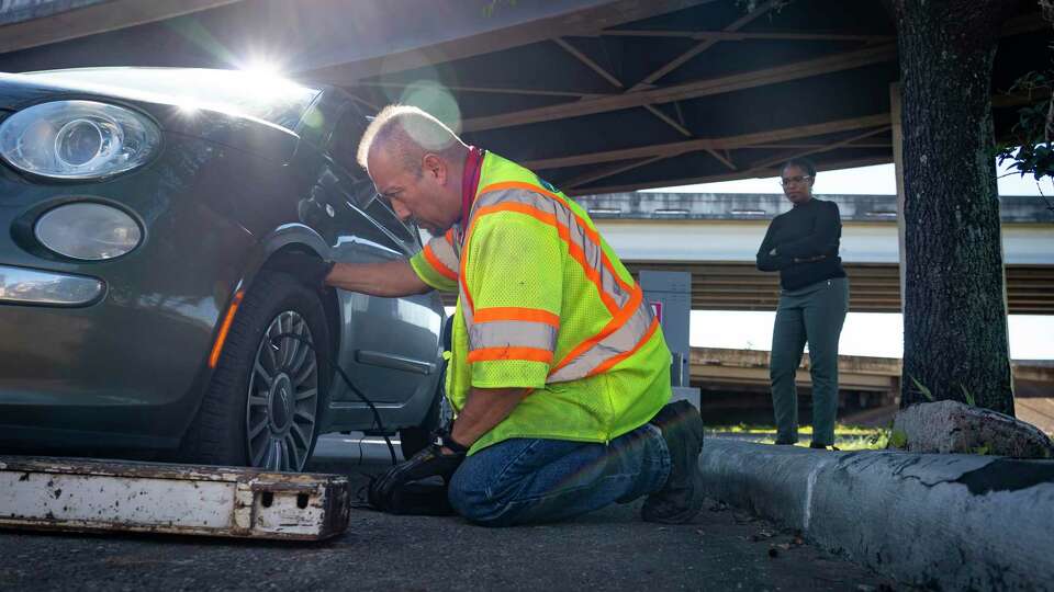 Tow and Go driver Rico Luna sees if he can fix the flat tire of driver Jasmine Hawkins' car after pulling her to a safe place after she pulled over onto the northbound shoulder of 288 with a flat tire, Thursday, Jan. 13, 2022, near downtown Houston. Hawkins was in the process of calling her insurance company for a tow when Luna pulled up and told her that she could get a free tow off of the freeway. 