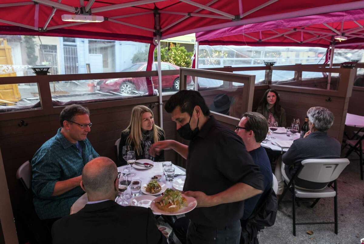 A waiter serves food to a table of guests at Terzo restaurant in their outdoor space. Data from OpenTable shows that restaurant reservations are beginning to rebound after the Omicron surge.