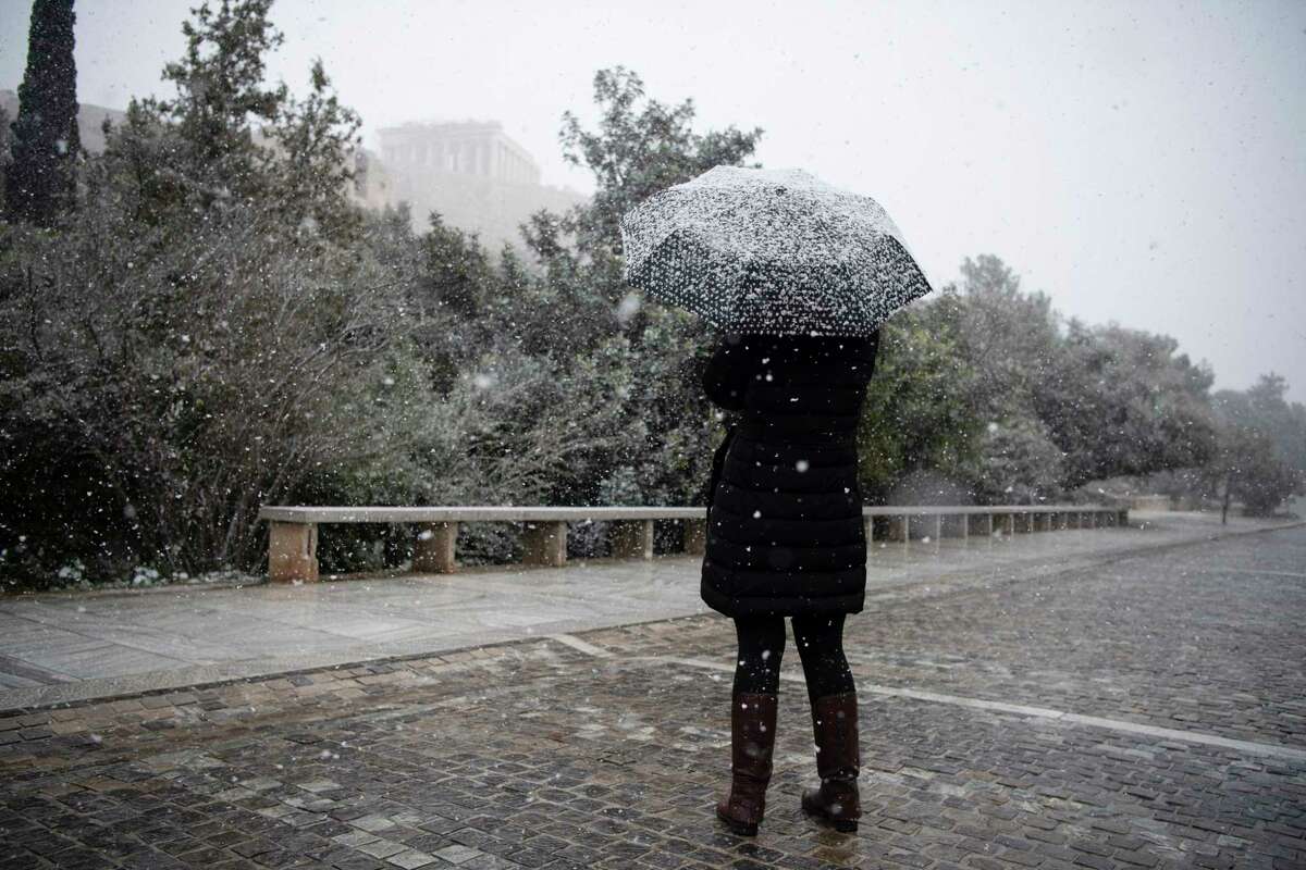 A woman with an umbrella stands as at the background is seen the ancient Parthenon temple during a snowfall, in Athens, on Monday, Jan. 24, 2022. The wave of bad weather hitting Greece is forecast to continue through Tuesday, and has seen snow falling even on some islands. Authorities have warned the public to avoid all but essential outdoor movement, and several major roads and highways are passable only with snow chains. AP Photo/Michael Varaklas)