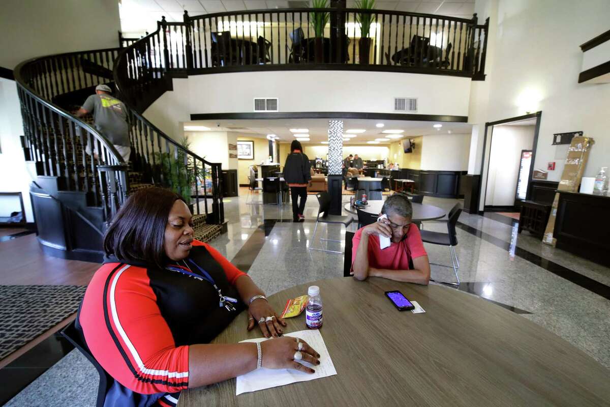 Harmony House employee Angela Perry, left, and resident Miriam Lopez, right on the phone, in the main lobby turned common room at the city’s first Navigation Center, a revamped hotel that temporarily houses homeless displaced from decommissioned tent encampments Friday, Nov. 19, 2021 in Houston.