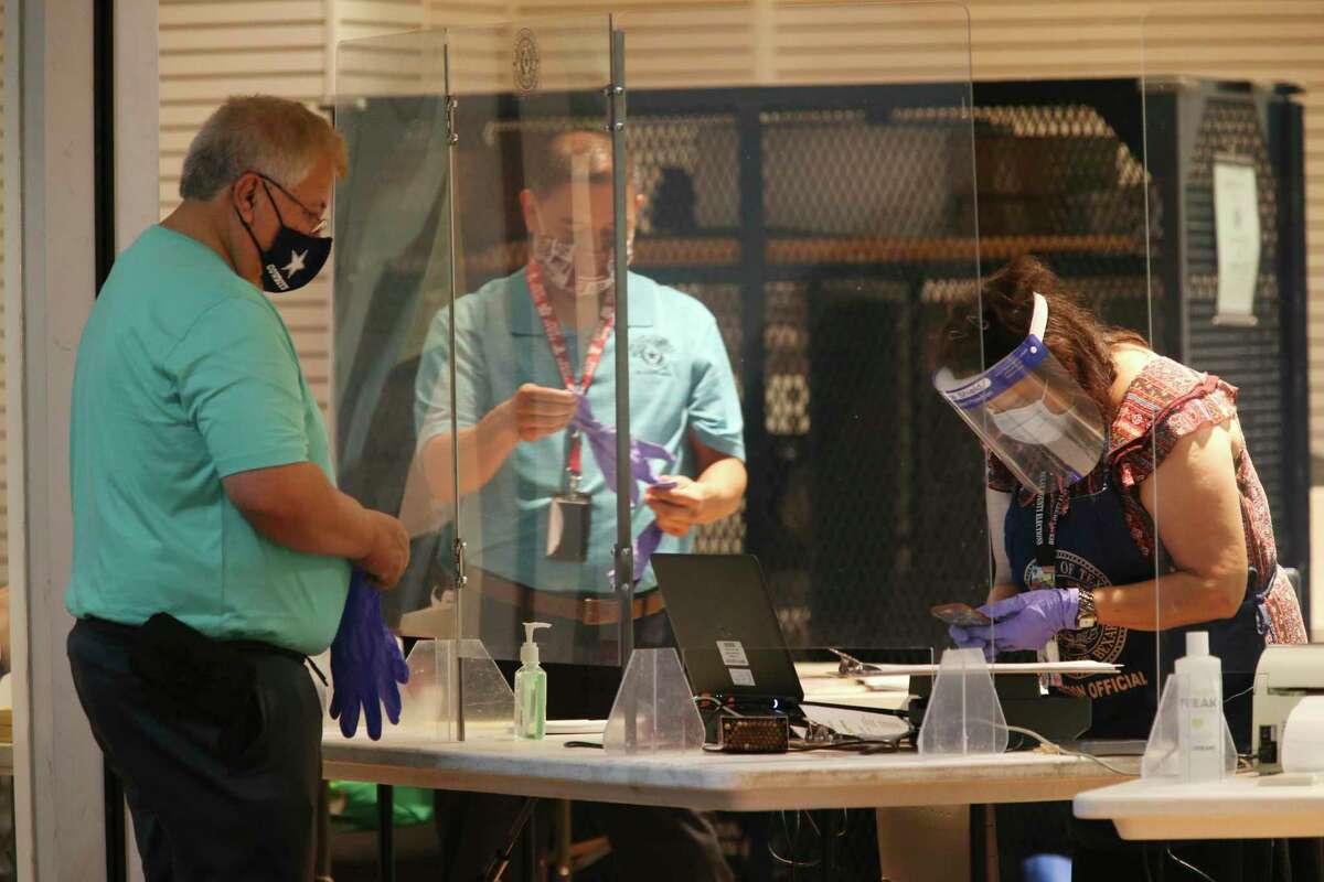 Poll workers wear protective gear as a man puts on gloves before voting at the Wonderland of the Americas Mall polling site on the first day of early voting in a 2020 primary runoff. The COVID-19 omicron variant now is posing a challenge to secure early voting sites for the March 1 primary, Elections Administrator Jacque Callanen told Bexar County commissioners Tuesday.