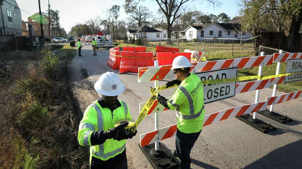 Gabe Wayne, left, and Gerardo Murillo, both with Houston Public Works, block off a street near a large sinkhole Wednesday, Jan. 26, 2022, in the 2500 block of Paul Quinn St., in the Acres Homes neighborhood in Houston.