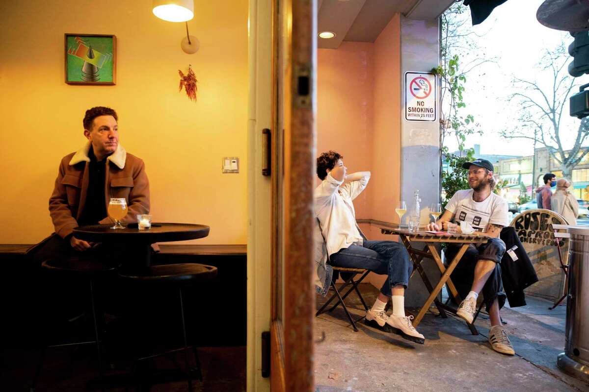 Aaron Curtis (left) drinks indoors as Leena Joshi and Brian Bartz and drink outdoors at Roses’ Taproom in Oakland.