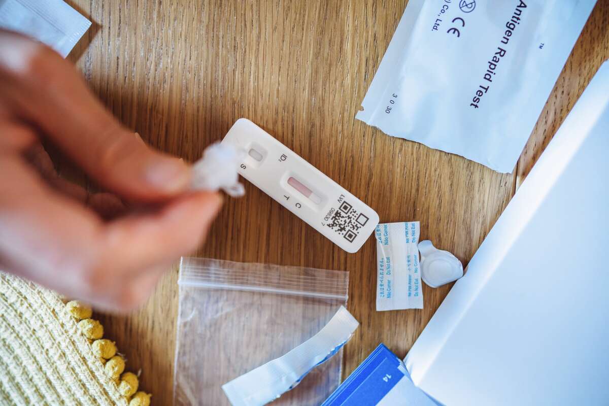 A woman squeezing the sample liquid on a test strip while carrying out a COVID-19 rapid self test at home. 