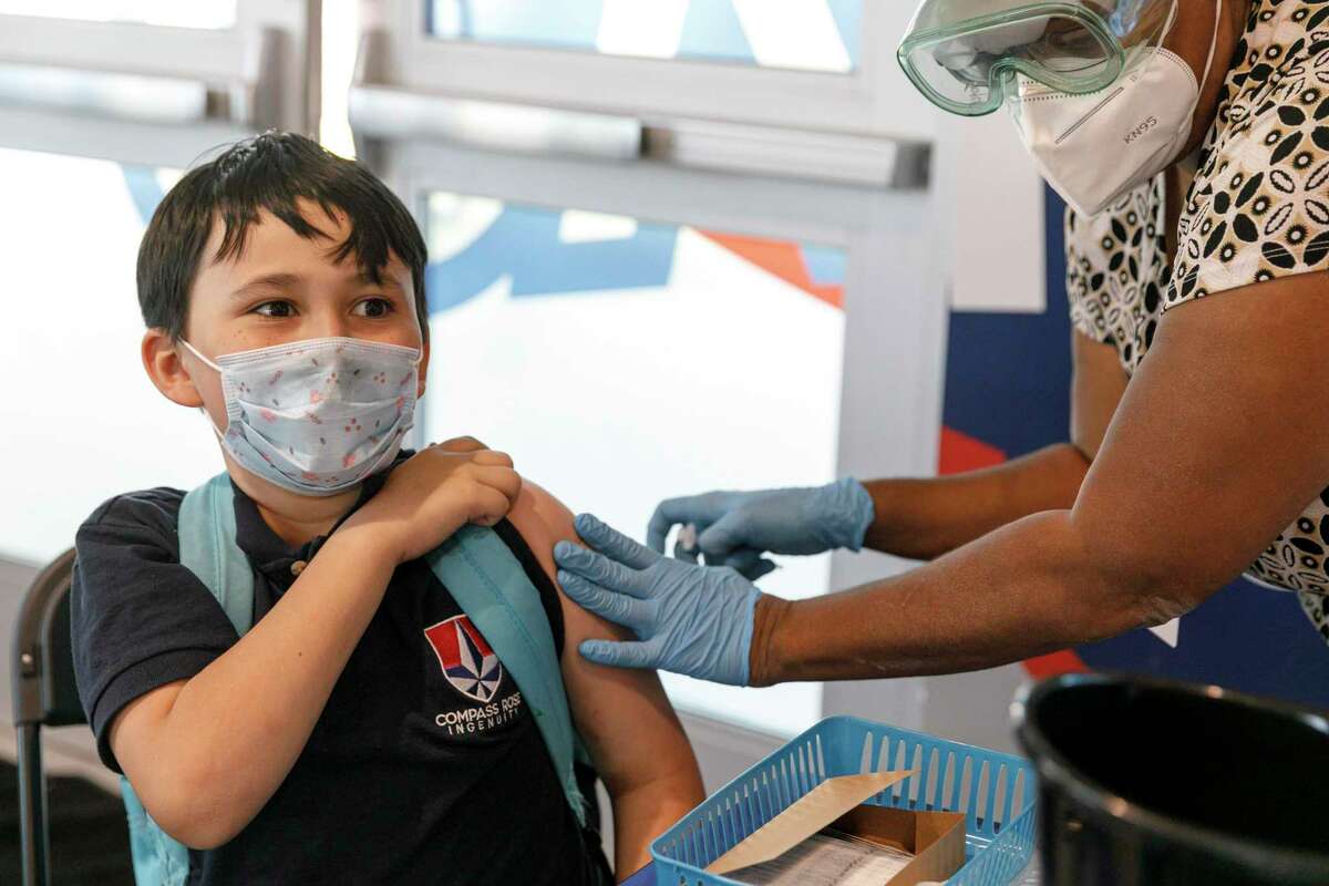 Richard Talamantez, 9, reacts after receiving his first dose of the Pfizer COVID-19 vaccine from registered nurse Joyce Turner during a free drive-up vaccine clinic at Compass Rose Ingenuity Campus Charter School in San Antonio, Texas, Wednesday afternoon, Jan. 5, 2022. After being dismissed from school at Compass Rose, he and his twin sister Amelia, not pictured, met their mother in the cafeteria to sign up for their shots.
