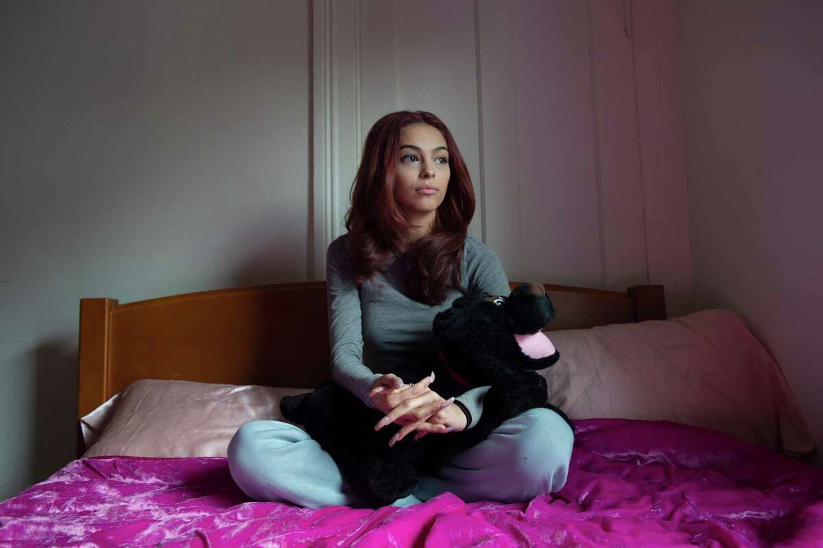 Emily Kenricks, 18, sits on the bed in her apartment in a transitional living home in Meriden, December 7, 2021.