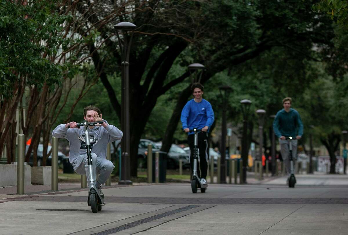 A trio of friends ride scooters through Hemisfair.