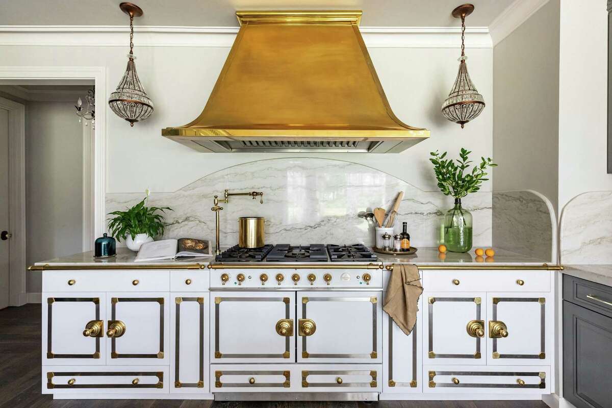 This showstopper wall in the kitchen of Brenda and Rodney Pennington has a La Cornue range, flanked by cabinets made and finished to look just like the range. They have a high-gloss finish mixed to match the range, and brass strappings and knobs purchased from La Cornue. The brass range hood was made by Lonestar Range Hood company in Houston.