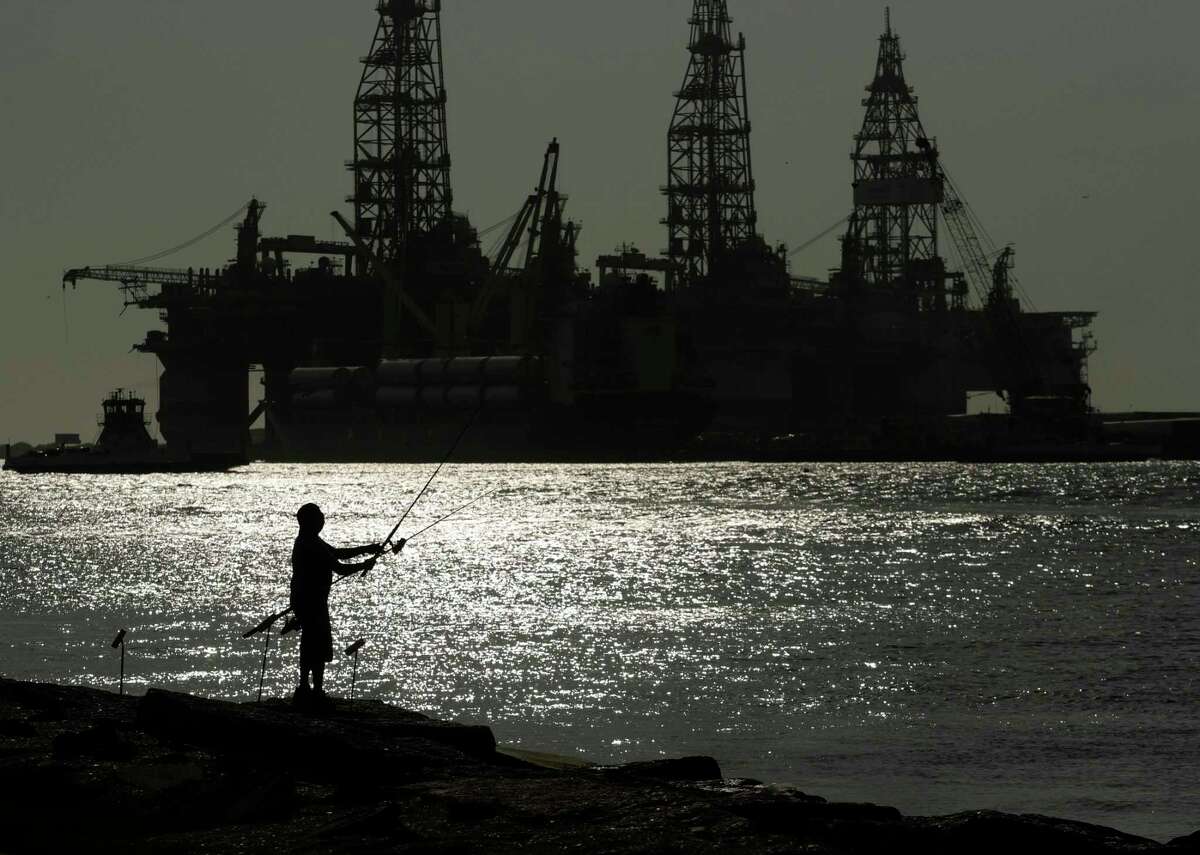 FILE - A man wears a face mark as he fishes near docked oil drilling platforms, on May 8, 2020, in Port Aransas, Texas. (AP Photo/Eric Gay, File)