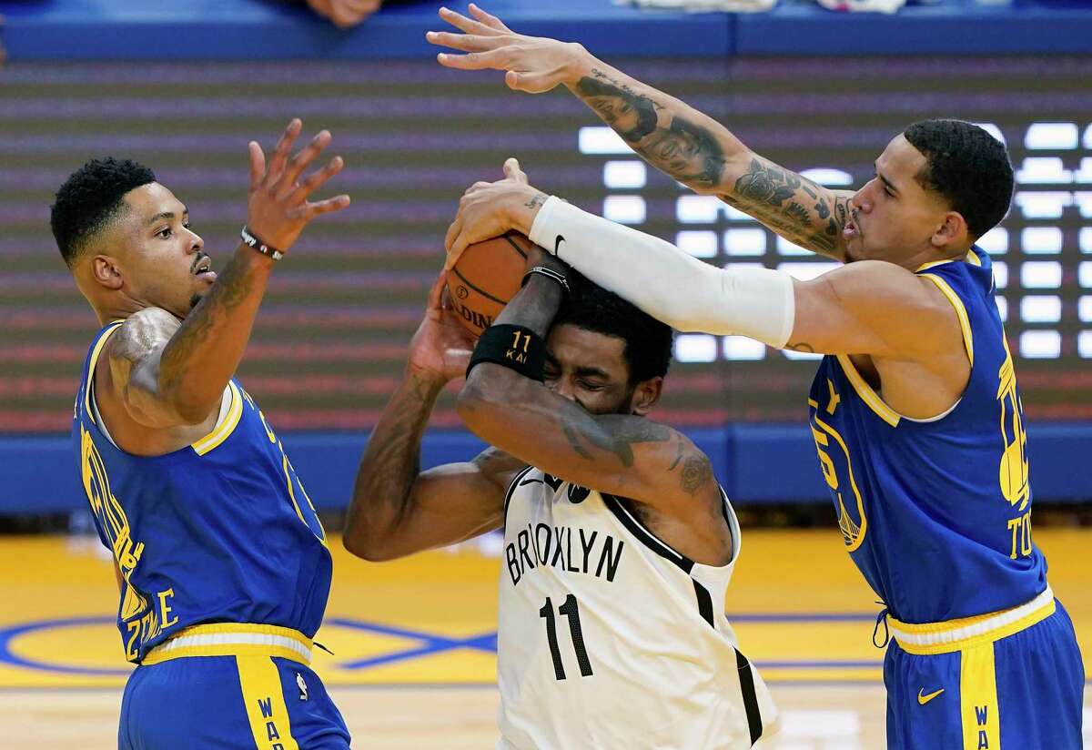 Kyrie Irving of the Nets fights to keep the ball away from Warriors defenders during a game 2021 at Chase Center