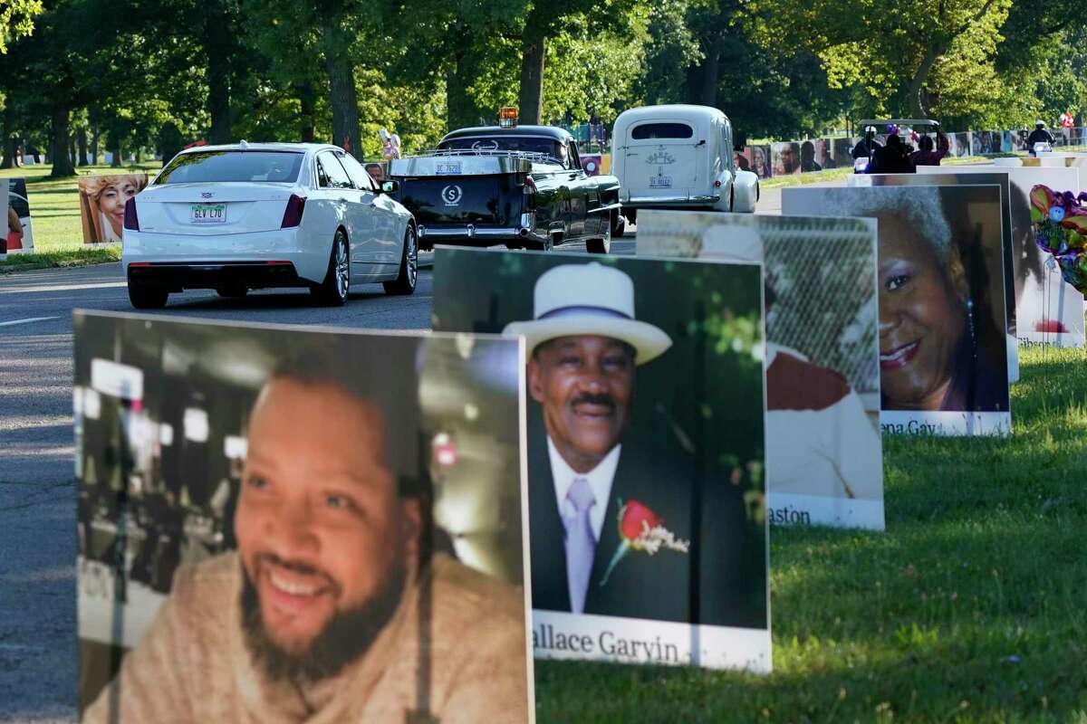 A procession of vehicles drive past photos of Detroit victims of COVID-19, Monday, Aug. 31, 2020 on Belle Isle in Detroit. Families have a chance to take one last public look at their lost loved ones in the nation's first citywide memorial to honor victims of the pandemic. Mourners will join 14 consecutive funeral processions to drive past nearly 900 large poster-sized photos of their loved ones staked around the island. (AP Photo/Carlos Osorio)