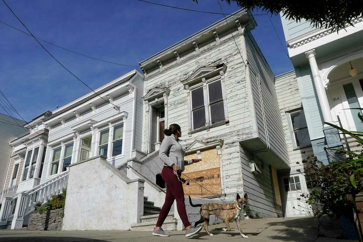 A pedestrian walks a dog past a recently sold Victorian home in San Francisco, Friday, Jan. 14, 2022. The decaying, 122-year-old Victorian marketed as “the worst house on the best block” of San Francisco sold for nearly $2 million in an auction, underscoring how tight the city’s housing market is and why one local politician is considering a tax that could push 4,000 currently vacant homes to the rental market in the next two years.