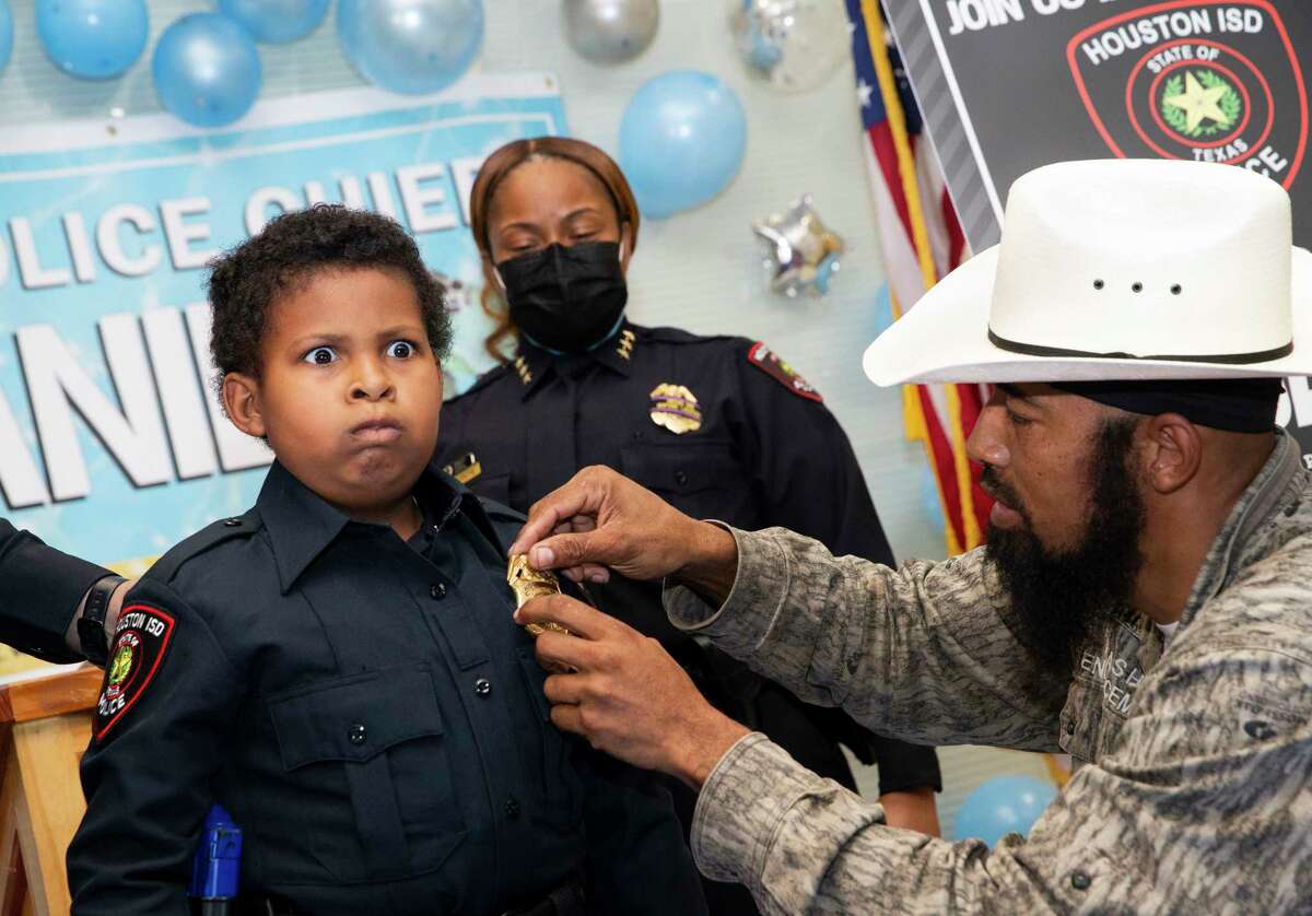 Ten-year-old Devarjaye “DJ” Daniel jokes that he has to put on a patrol officer’s face as his father, Theodis Daniel, is pinning his honorary Houston ISD police chief badge during a swear-in ceremony Monday, Jan. 31, 2022, at HISD Police Headquarters in Houston. DJ has terminal brain and spinal cancer and wants to be sworn into 100 law enforcement agencies to raise awareness to childhood cancer.