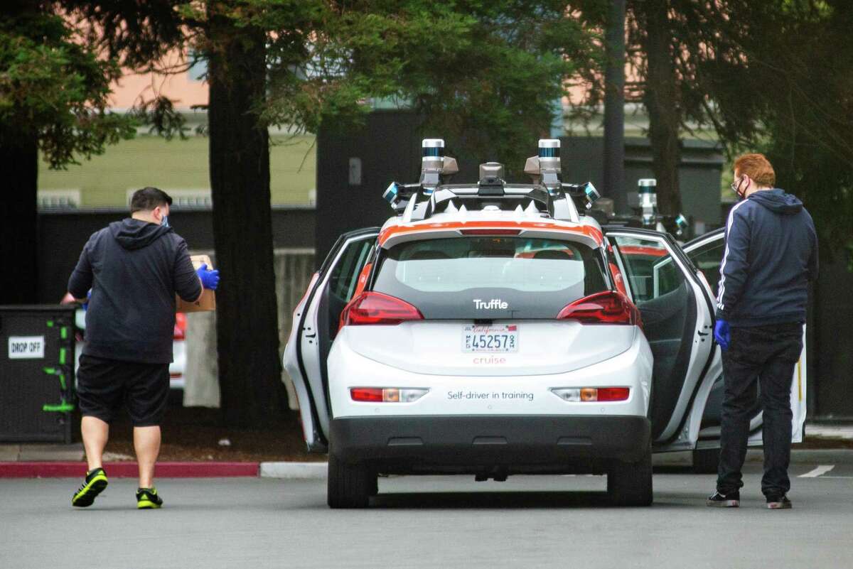 Cruise employees carrying packages out of an autonomous car at a Cruise facility in San Francisco, in 2020.