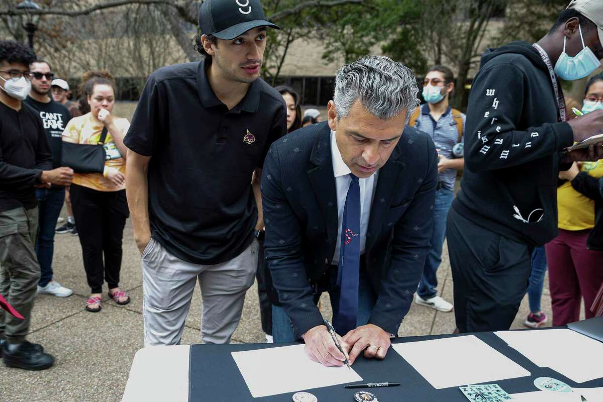 Hays County Judge Ruben Becerra, front, and his son Cristian Becerra sign a petition to put cannabis decriminalization on the November ballot for San Marcos residents on the Quad of Texas State University in San Marcos, Texas, Tuesday, Feb. 1, 2022. Before signing the petition, Judge Becerra spoke to students at a press conference held by Mano Amiga, an organization that fights for criminal justice and immigration reform, about his support for the initiative.