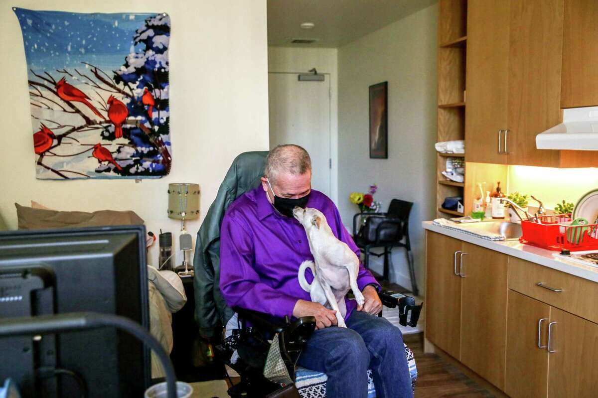 Timothy Isaiah sits with his dog, Kelly, in his studio in the new modular housing complex on Bryant Street.