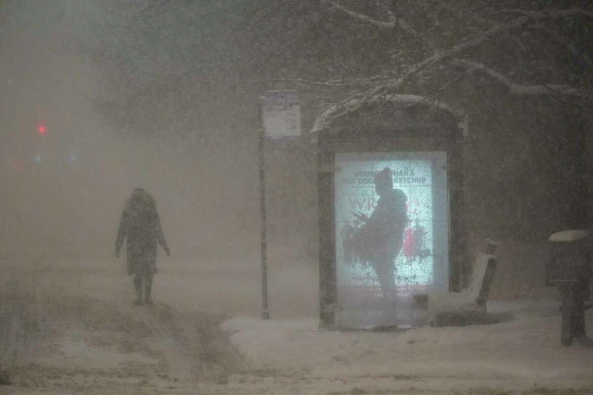 A woman walks to a bus shelter on Dr. Martin Luther King Drive as a man waits in the shelter during the pre-dawn hours Wednesday, Feb. 2, 2022, in Chicago. A major winter storm with millions of Americans in its path brought a mix of rain, freezing rain and snow to the middle section of the United States as airlines canceled hundreds of flights, governors urged residents to stay off roads and schools closed campuses.