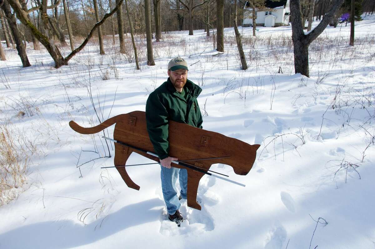 Adam Bump, a wildlife biologist with the Michigan Department of Natural Resources Cougar Team, poses with a cutout of a cougar used for research by the Wildlife Biology division. 