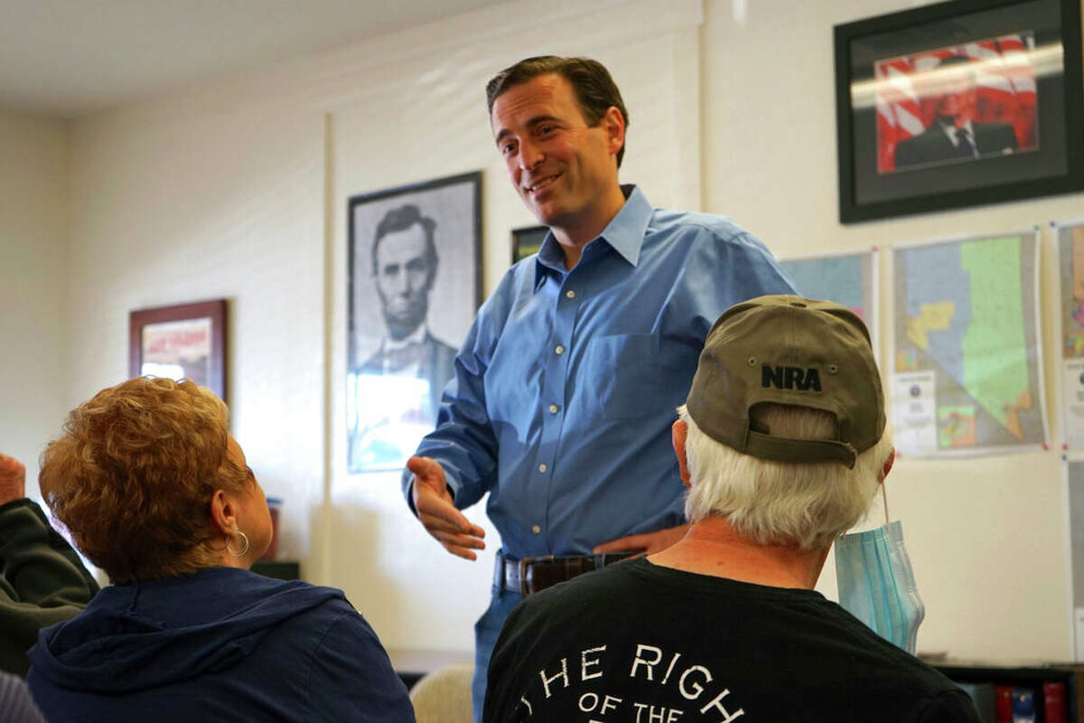 In this photo taken Oct. 10, 2021, Republican Adam Laxalt, flanked by pictures of Presidents Abraham Lincoln and Ronald Reagan, talks to a supporter at the Douglas County Republican Party headquarters on the final day of his Senate campaign's statewide tour in Gardnerville, Nev. 