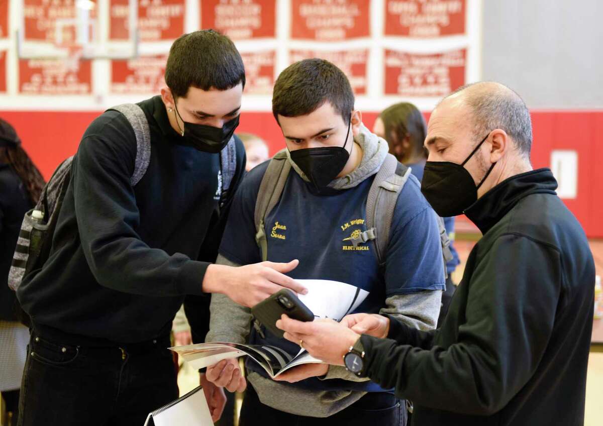 Students Luis Olea, left, and Juan Senna, center, chat with InnerSpace Electronics Project Manager Rocco Rutigliano at the Home Builders and Remodelers Association of Fairfield County job fair at J.M. Wright Technical High School in Stamford, Conn. Wednesday, Feb. 2, 2022. Job-seeking trade students met with employers in a first-of-its-kind event intended to inform students of different job opportunities and hire on the spot.